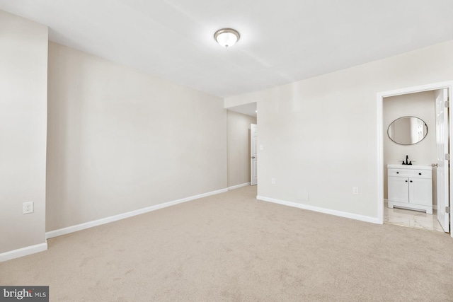 unfurnished bedroom with light colored carpet, connected bathroom, a sink, and baseboards