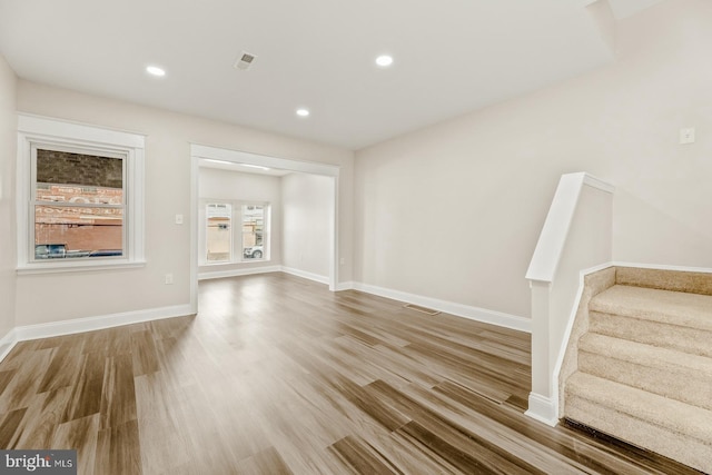 unfurnished living room with stairs, recessed lighting, baseboards, and wood finished floors