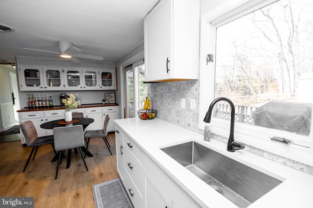 kitchen with a sink, white cabinets, glass insert cabinets, light wood-style floors, and backsplash