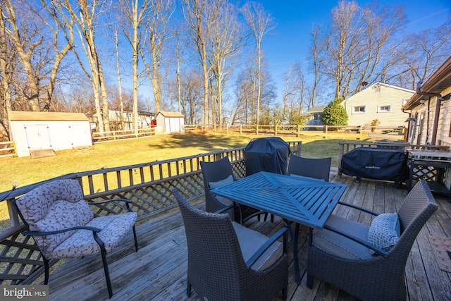 wooden terrace with a lawn, outdoor dining area, a fenced backyard, an outbuilding, and a storage unit