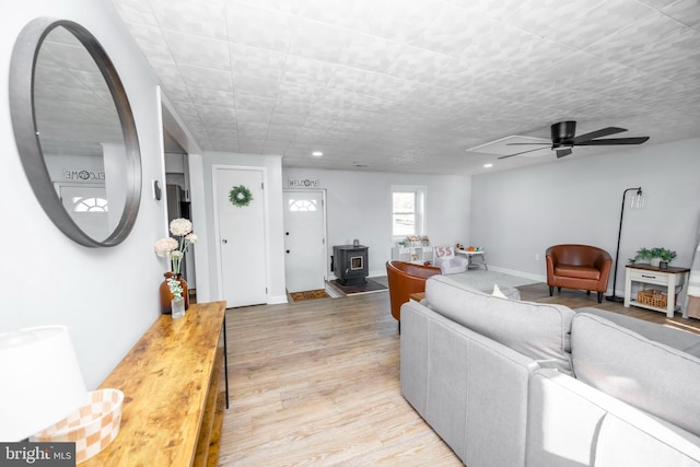 living area featuring a ceiling fan, baseboards, a wood stove, light wood-style flooring, and recessed lighting