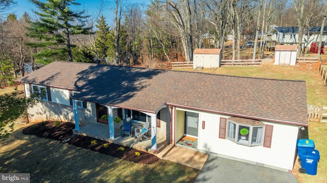 view of front of house featuring a shingled roof, a storage unit, a patio, and an outdoor structure