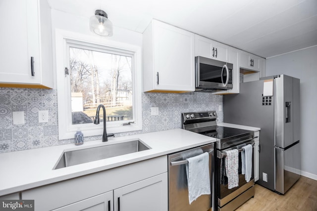 kitchen with a sink, decorative backsplash, light countertops, white cabinets, and appliances with stainless steel finishes