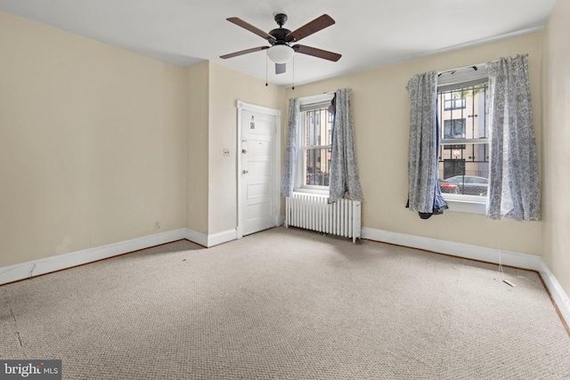 carpeted spare room with radiator, baseboards, and a ceiling fan