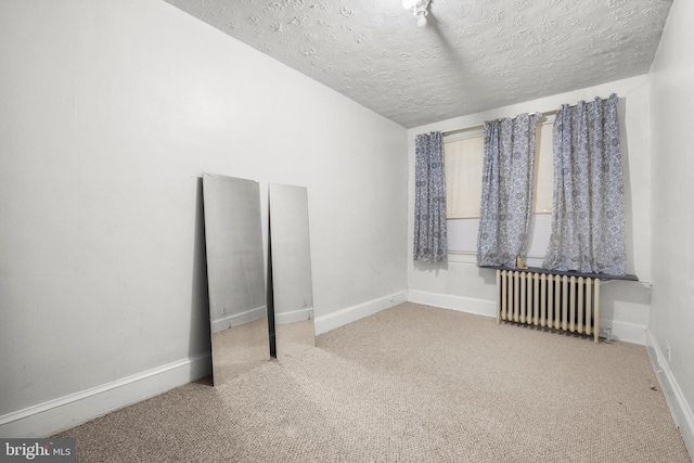 carpeted empty room with a textured ceiling, baseboards, and radiator