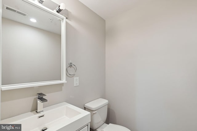 half bathroom with vanity, toilet, and visible vents