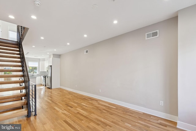 unfurnished living room with visible vents, recessed lighting, light wood finished floors, baseboards, and stairs