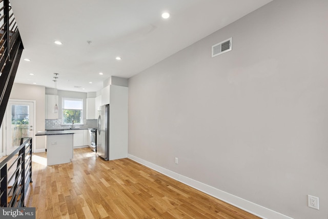 kitchen featuring visible vents, light wood-style flooring, white cabinets, dark countertops, and backsplash