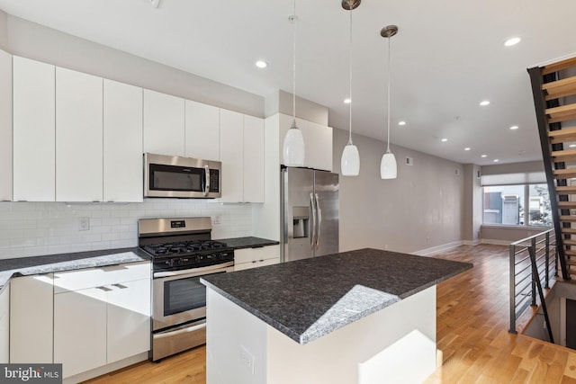 kitchen with a kitchen island, stainless steel appliances, light wood-style floors, decorative backsplash, and hanging light fixtures