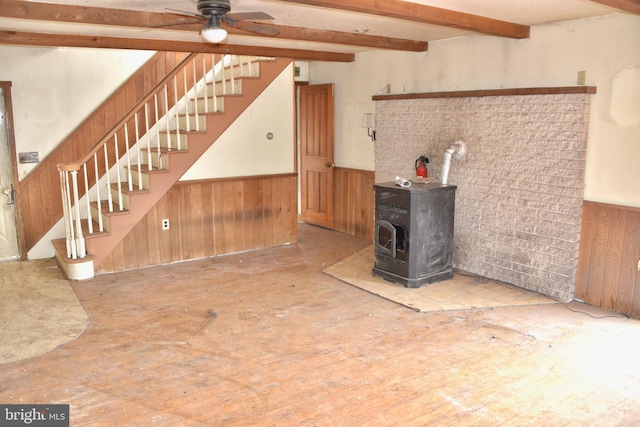 unfurnished living room with beam ceiling, a wainscoted wall, wood walls, and a wood stove