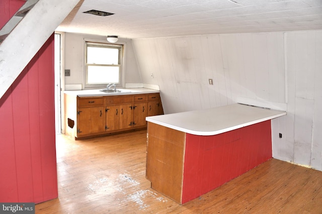 kitchen featuring brown cabinets, light countertops, a sink, light wood-type flooring, and a peninsula