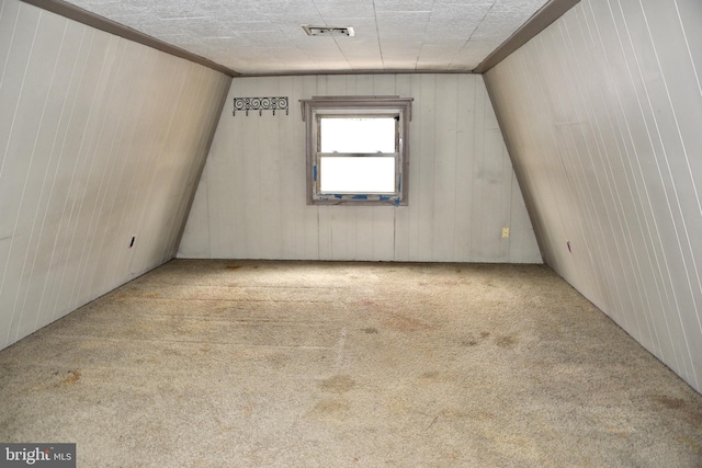 unfurnished room featuring vaulted ceiling, carpet floors, wood walls, and visible vents