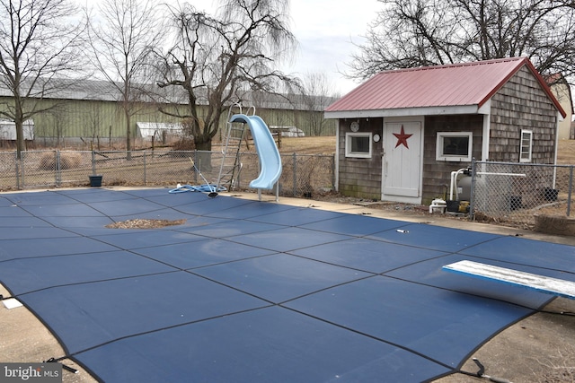 view of swimming pool with a storage shed, an outbuilding, fence, a water slide, and a diving board