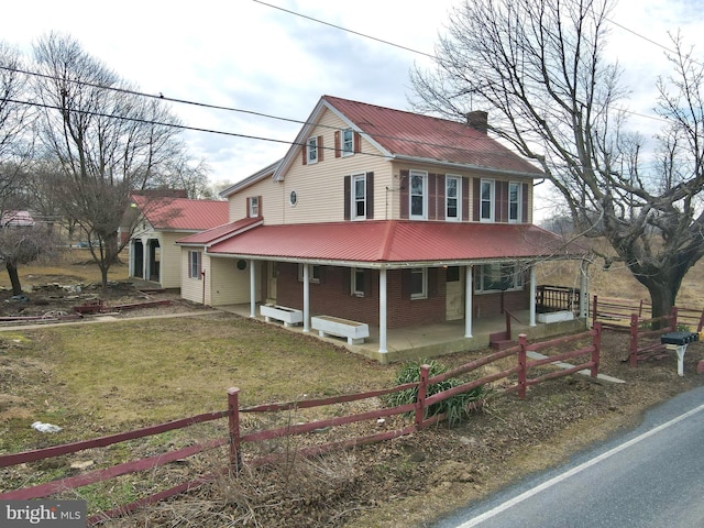 country-style home with a chimney, covered porch, fence, metal roof, and a front lawn