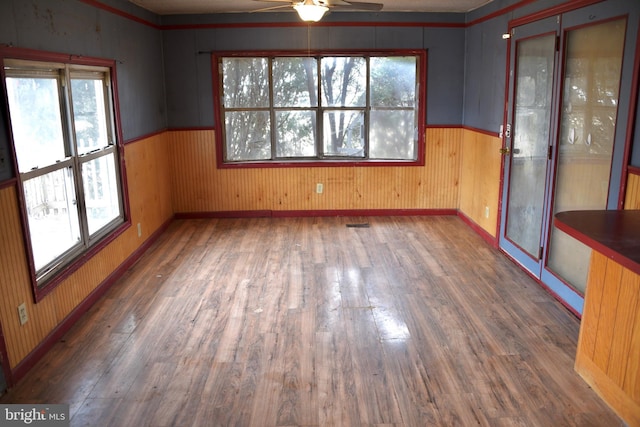 spare room with a healthy amount of sunlight, a wainscoted wall, a ceiling fan, and wood finished floors