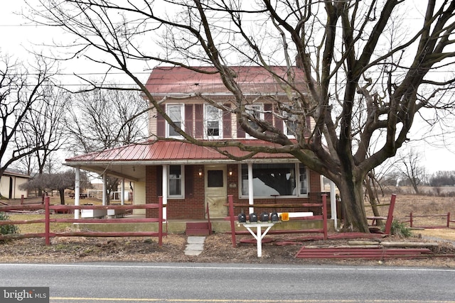 view of front of property featuring metal roof, brick siding, a fenced front yard, and a porch