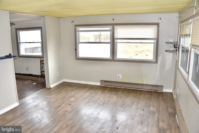 empty room with baseboard heating, wood finished floors, and a healthy amount of sunlight