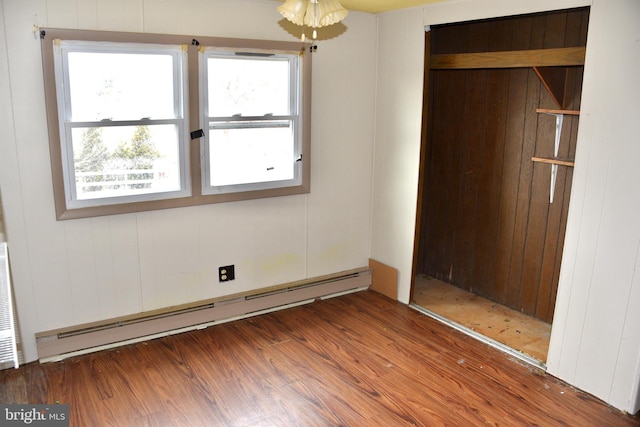 unfurnished bedroom featuring a baseboard heating unit, a closet, and wood finished floors