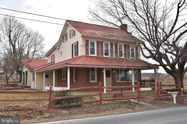 country-style home featuring metal roof, a porch, a fenced front yard, and brick siding