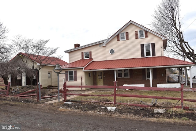 view of front of home featuring a chimney, metal roof, covered porch, fence, and brick siding