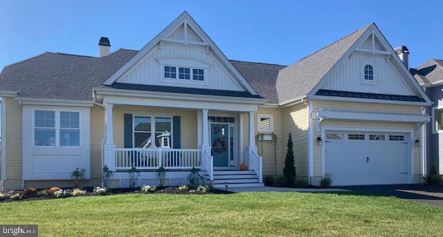 view of front of house featuring a standing seam roof, covered porch, driveway, a chimney, and a front yard