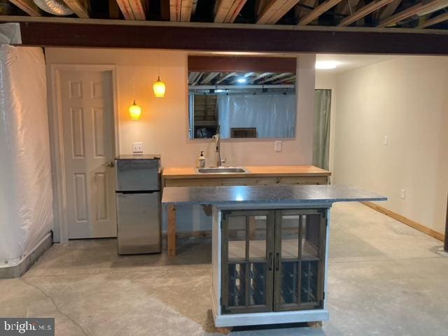 bar with freestanding refrigerator, a sink, baseboards, and unfinished concrete floors