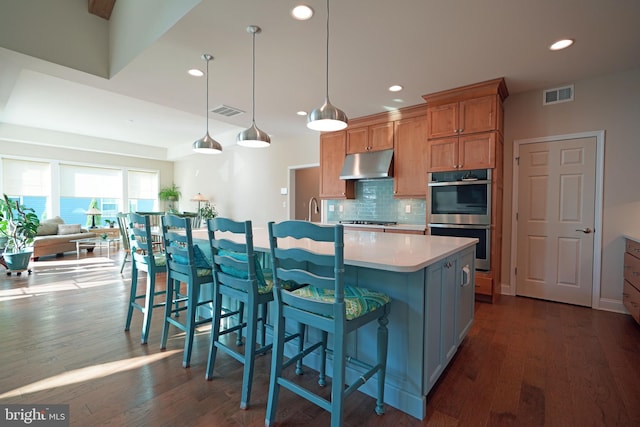 kitchen featuring stainless steel appliances, visible vents, under cabinet range hood, and decorative backsplash