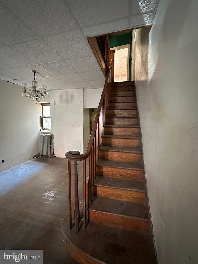 staircase featuring radiator heating unit, a chandelier, concrete flooring, and a drop ceiling