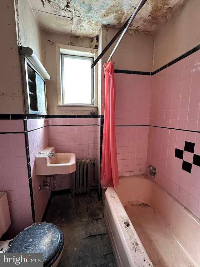 full bath with tile walls, radiator, shower / bath combo with shower curtain, wainscoting, and a sink