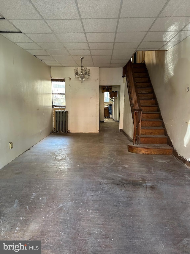 unfurnished living room featuring a chandelier, a paneled ceiling, stairs, radiator heating unit, and unfinished concrete flooring