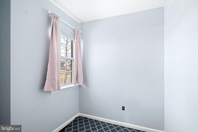 spare room with baseboards and dark carpet