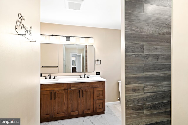 full bathroom featuring marble finish floor, double vanity, a sink, and toilet