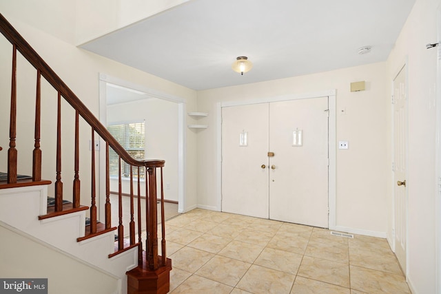 foyer entrance featuring light tile patterned floors, stairway, visible vents, and baseboards