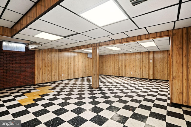 finished basement with a paneled ceiling, visible vents, wood walls, and tile patterned floors