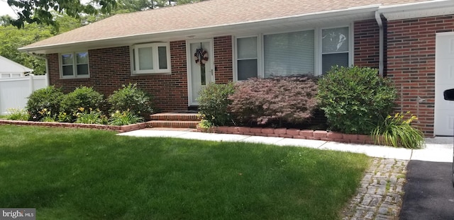 single story home featuring a shingled roof, a front yard, fence, and brick siding