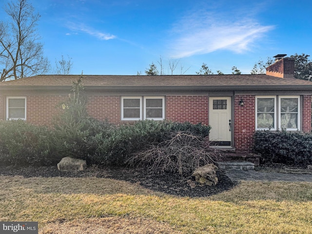 ranch-style home with a shingled roof, a front yard, brick siding, and a chimney