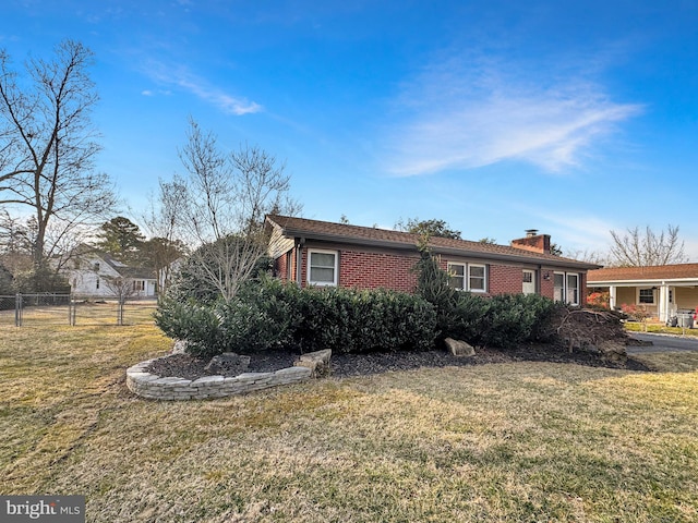 view of side of home with brick siding, a yard, a chimney, and fence