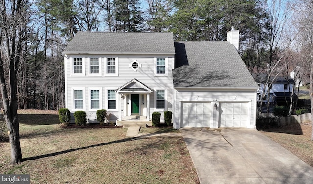 colonial inspired home featuring a shingled roof, a front yard, a chimney, driveway, and an attached garage