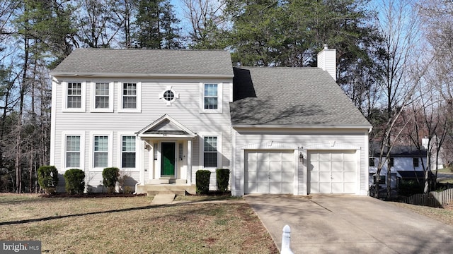 colonial-style house featuring concrete driveway, a front yard, roof with shingles, a chimney, and a garage