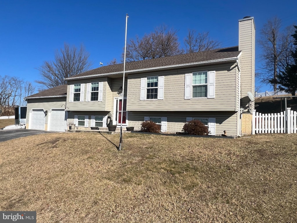 bi-level home featuring aphalt driveway, an attached garage, fence, a chimney, and a front yard