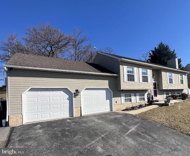 bi-level home with entry steps, a shingled roof, a chimney, aphalt driveway, and an attached garage