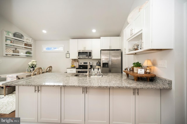 kitchen with stainless steel appliances, a peninsula, a sink, white cabinets, and light stone countertops