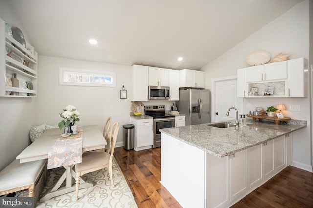 kitchen featuring light stone counters, stainless steel appliances, white cabinetry, a sink, and a peninsula