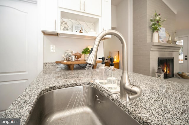 details with light stone countertops, a fireplace, white cabinets, and a sink