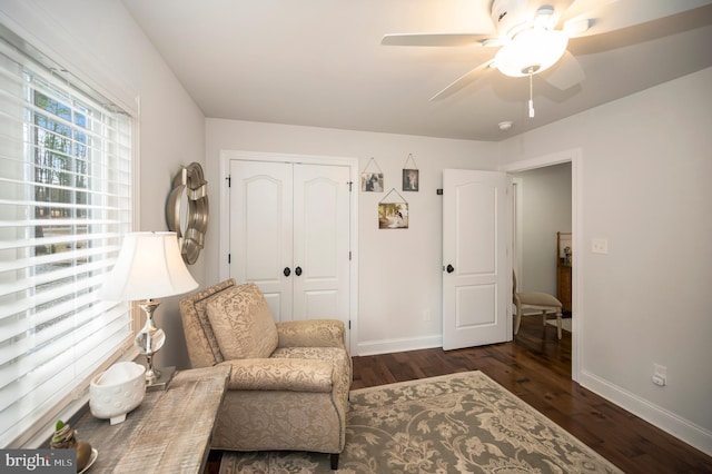 living area with a ceiling fan, baseboards, and dark wood-style flooring