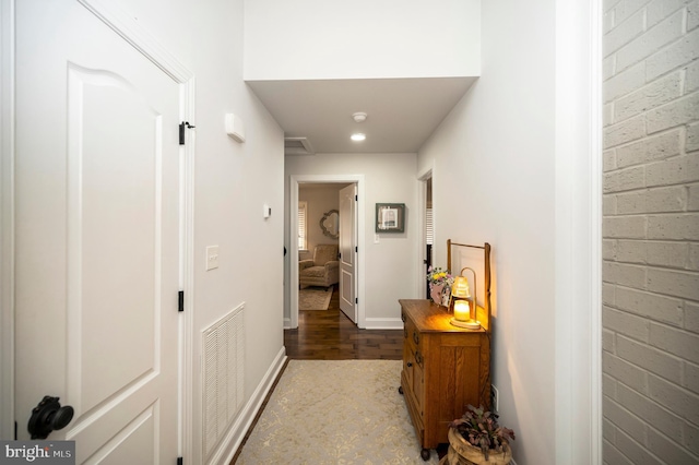 corridor with baseboards, visible vents, and brick wall