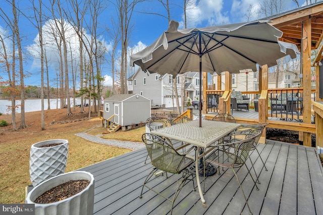 deck with outdoor dining area, a water view, an outdoor structure, and a storage shed