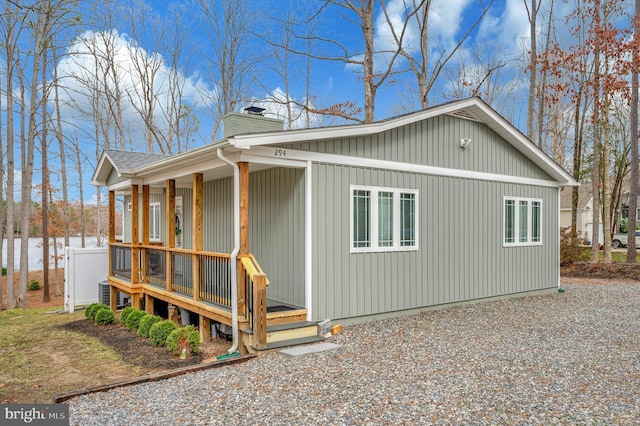 view of side of property featuring covered porch, a shingled roof, a chimney, and cooling unit