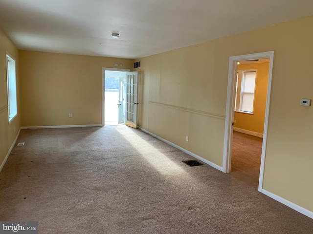 empty room with carpet floors, plenty of natural light, and visible vents