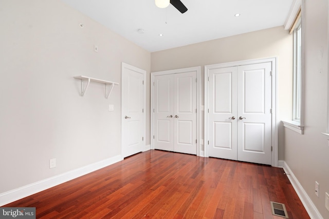 unfurnished bedroom featuring baseboards, wood-type flooring, visible vents, and two closets